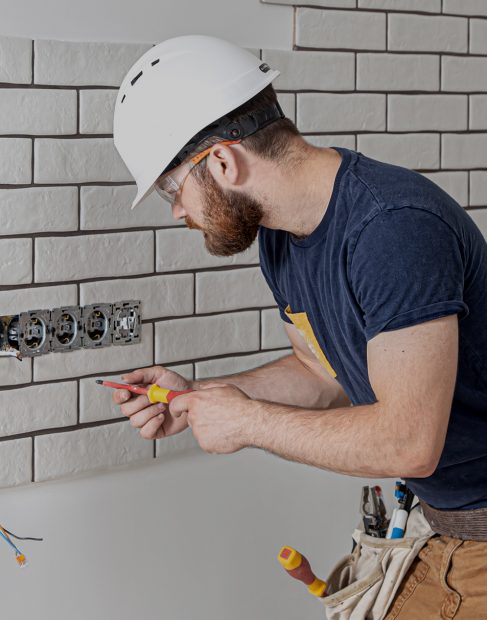 Electrician construction worker with a beard in overalls during the installation of sockets. Home renovation concept.